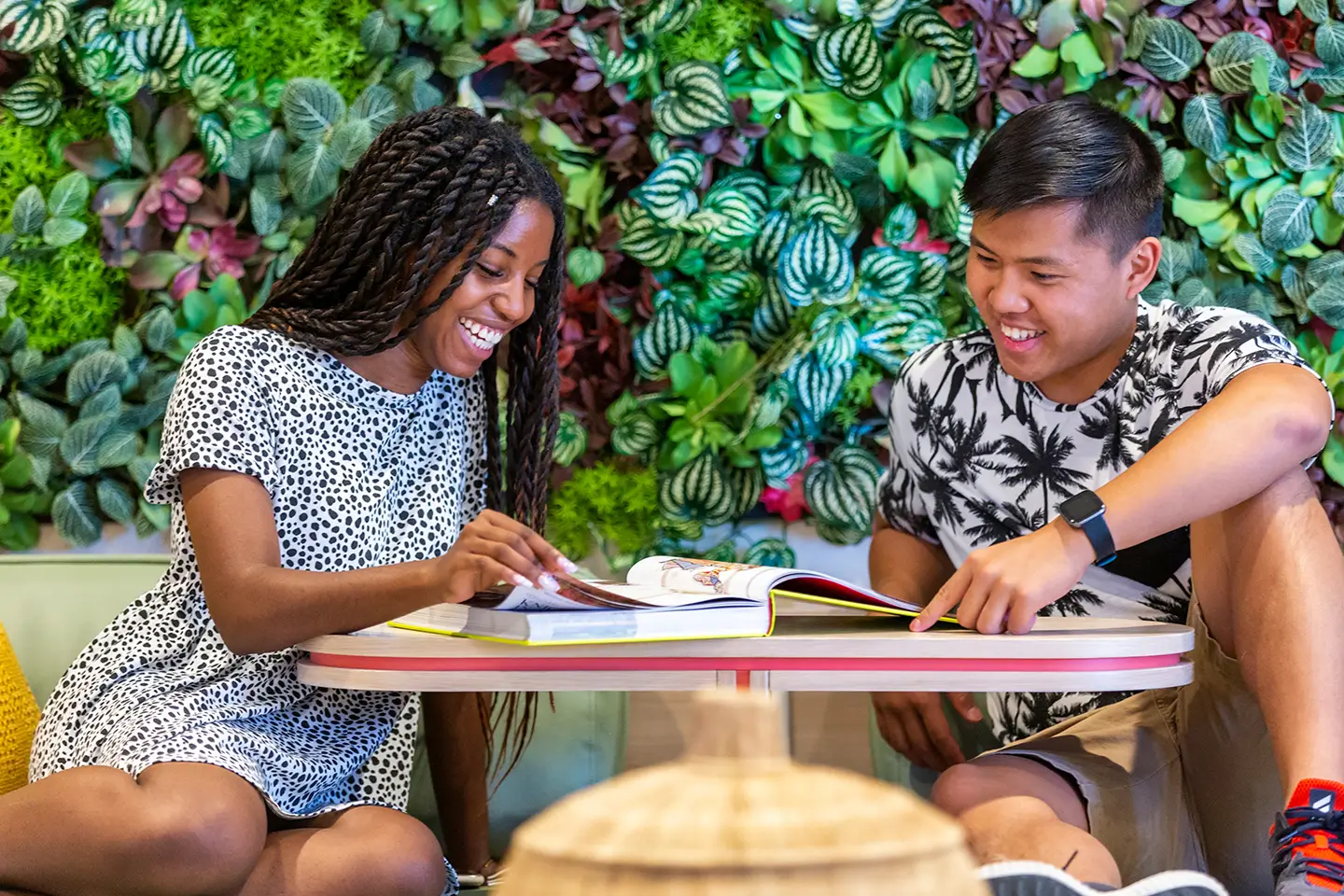 Two young adults reading a book at a shared table.